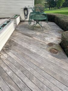 Weathered wooden deck with stacked green metal patio chairs against the house; planter boxes and a hose reel nearby.
